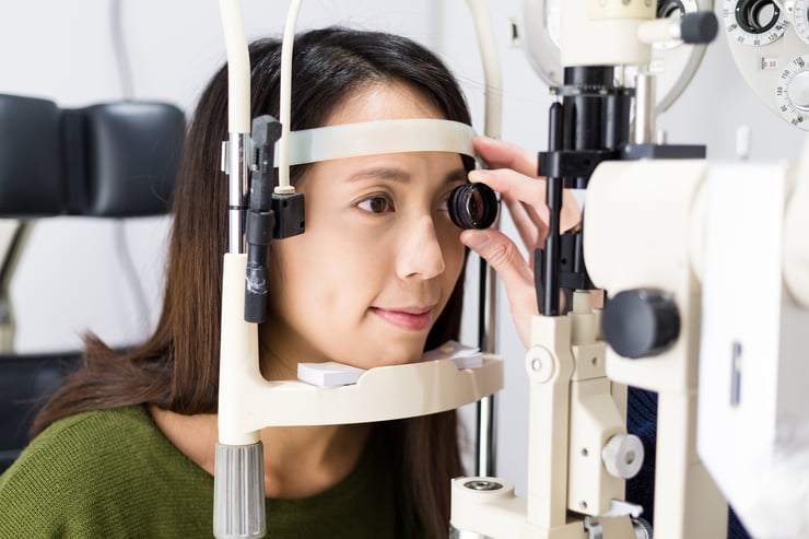 Asian woman receiving an eye exam with a tonometer at a clinic.